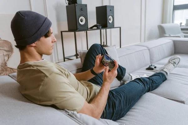 A person is resting on the sofa playing games on a mobile device