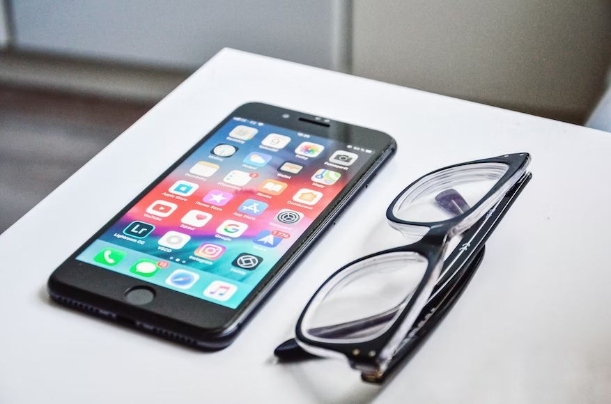 The image shows a pair of glasses and a mobile phone with many apps on the screen