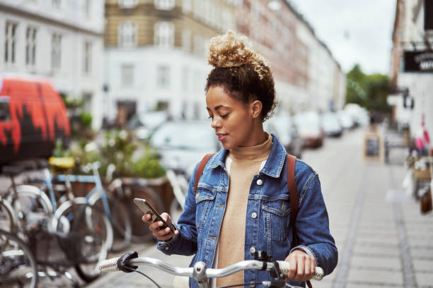 The image shows a person holding a mobile phone in her hands while she is outside sitting on her bike