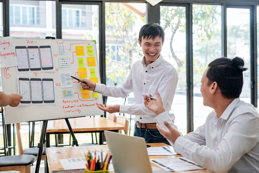The image shows a person in front of a whiteboard showing some analytics to another person