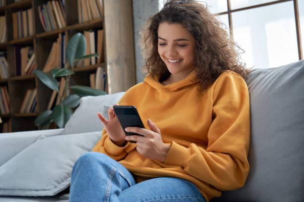 A person is holding a mobile phone while she is seated on the sofa