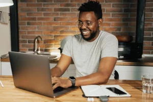 The image shows a person smiling in front of a laptop